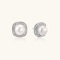 Rhodium-plated sterling silver stud earrings with round freshwater pearls surrounded by geometric crystal halos on cream background.