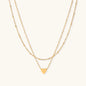 Delicate double-chain gold necklace with tiny heart pendant on cream background