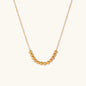 Delicate gold-plated necklace with graduated spherical beads forming gentle smile curve on beige background