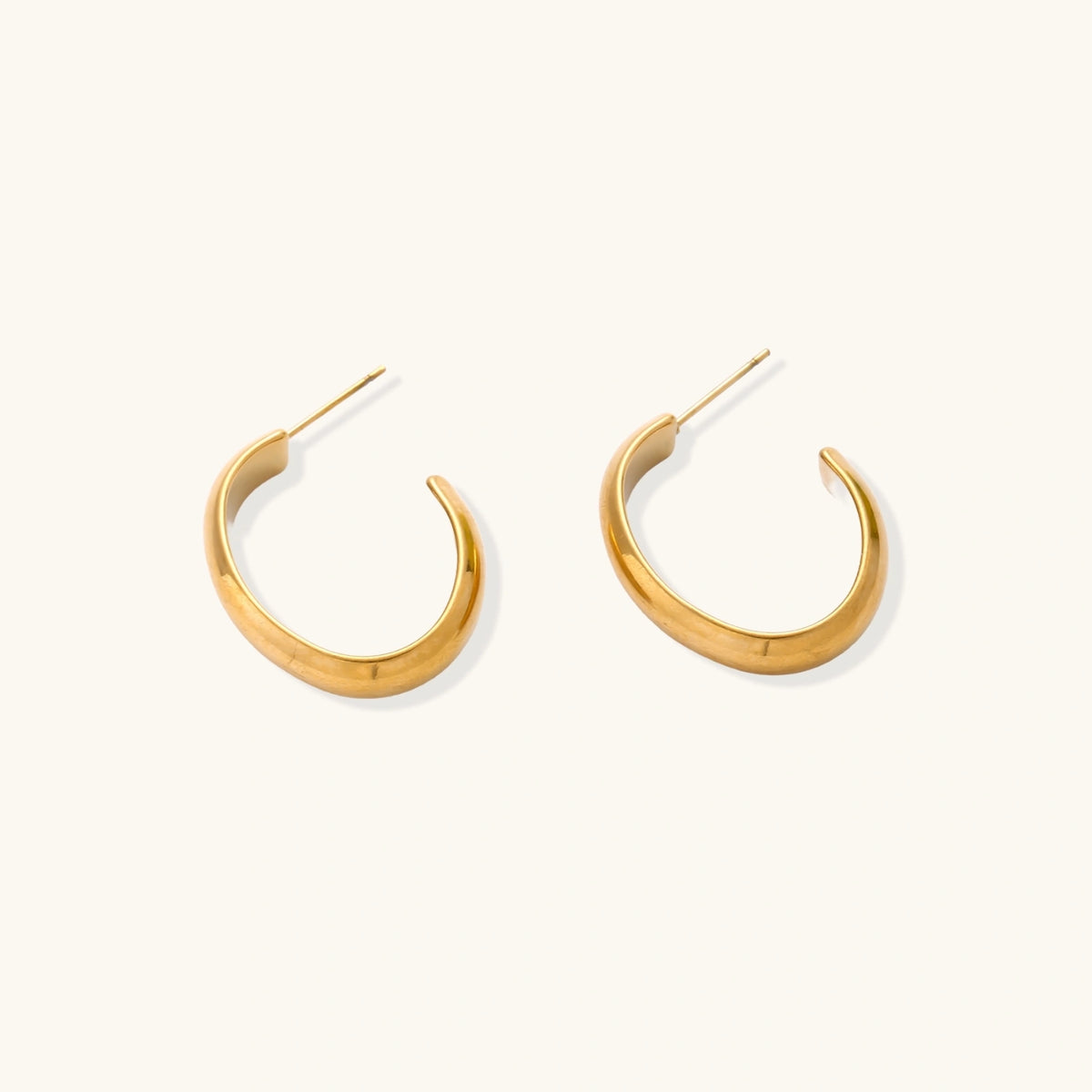 Chunky tubular hoop earrings in warm 14K gold-plated finish with smooth polished surface on cream background.