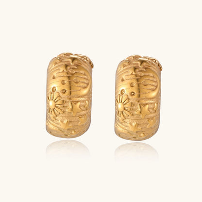 Wide gold hoop earrings with embossed stars and sun motifs on cream background, showing dimensional relief details.