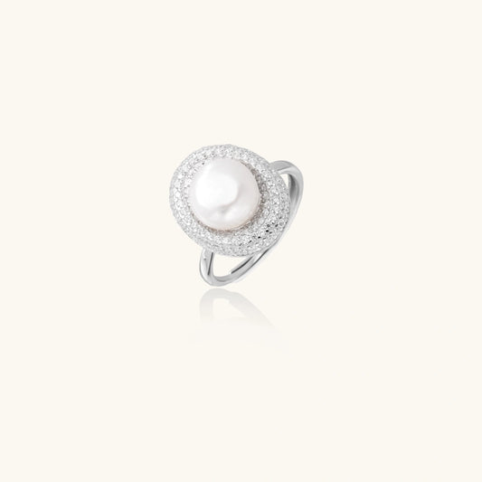 Silver ring with lustrous white pearl center surrounded by sparkling crystal halo on light background.