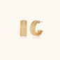 Textured gold huggie hoop earrings with raised ribbed rows creating dimensional sculptural design on cream background