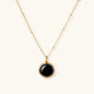 Circular black agate pendant on gold-plated sterling silver chain against cream background, showing modern minimalist design.