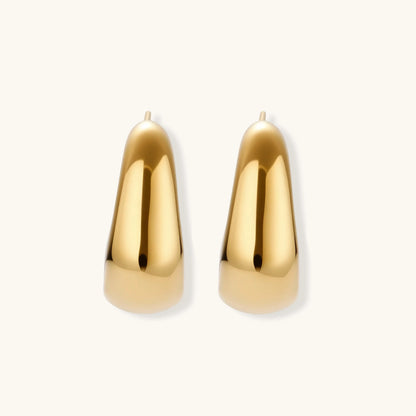 Close-up of curved gold-plated huggie earrings with sculptural design on white background, showing polished finish.