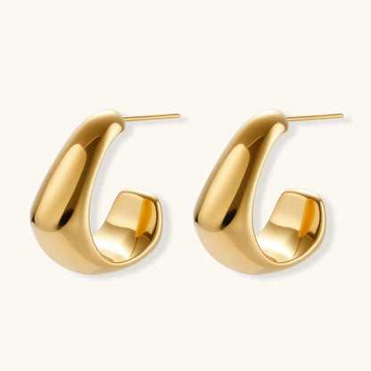 Close-up of curved gold-plated huggie earrings with sculptural design on white background, showing polished finish.
