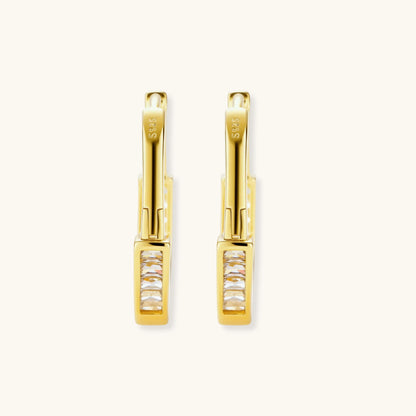 Close-up of gold-plated sterling silver huggie hoop earrings featuring rectangular cubic zirconia stones on neutral background.